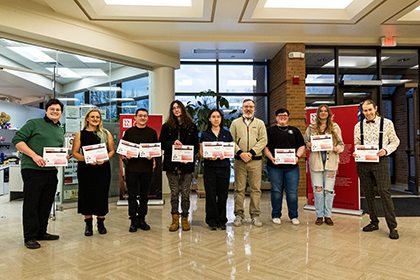 21st annual student award winners holding their certificates in the lobby surrounding Dept. chair blake johnson.